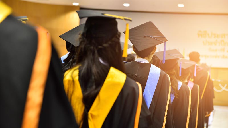 Students graduating are standing in a line to get their diplomas.