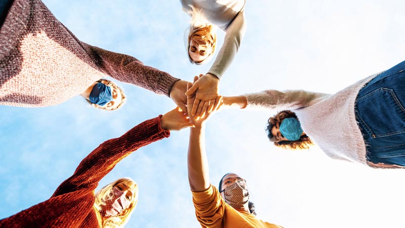 Five students with their hands stacked in the middle signifying a team.